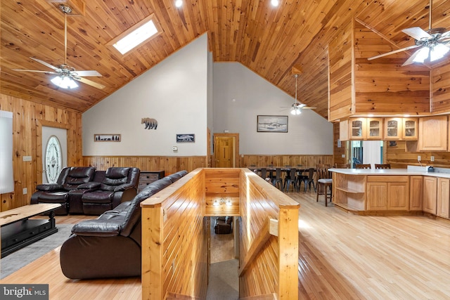 interior space featuring a skylight, light wood-type flooring, ceiling fan, kitchen peninsula, and high vaulted ceiling