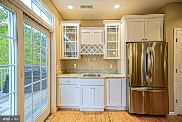 kitchen with white cabinetry, sink, and stainless steel refrigerator