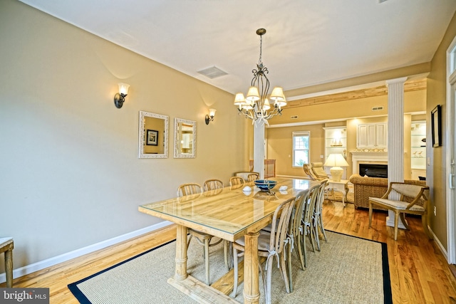 dining space with a notable chandelier, light wood-type flooring, and ornate columns