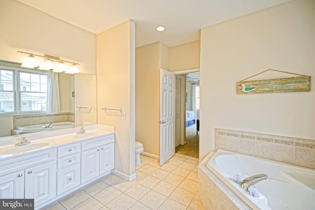 bathroom with a relaxing tiled tub, vanity, toilet, and tile patterned floors