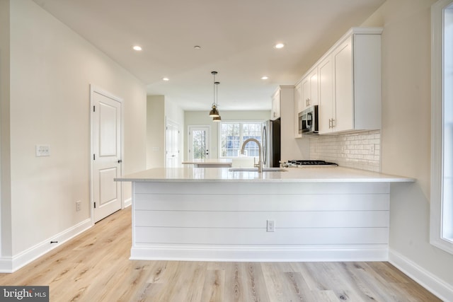 kitchen with light wood-type flooring, stainless steel appliances, white cabinetry, sink, and kitchen peninsula