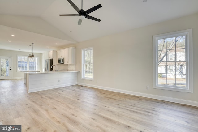 unfurnished living room featuring ceiling fan, sink, vaulted ceiling, and light hardwood / wood-style floors