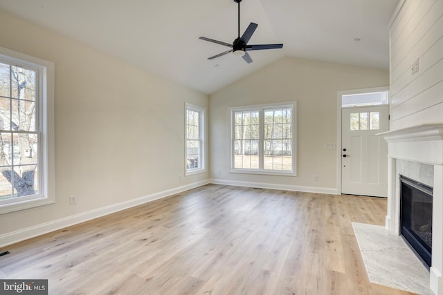 unfurnished living room featuring lofted ceiling, ceiling fan, a fireplace, and a healthy amount of sunlight