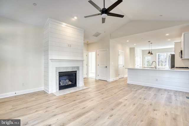 unfurnished living room featuring vaulted ceiling, a high end fireplace, light hardwood / wood-style flooring, sink, and ceiling fan