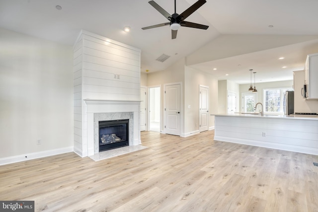 unfurnished living room with light hardwood / wood-style flooring, a premium fireplace, sink, ceiling fan, and lofted ceiling