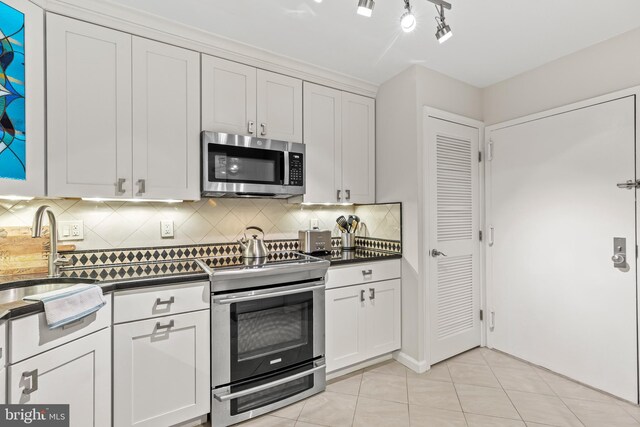 kitchen featuring appliances with stainless steel finishes, decorative backsplash, light tile patterned flooring, white cabinets, and sink