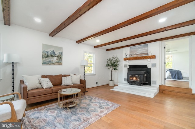 living room with light hardwood / wood-style flooring, beamed ceiling, and a wood stove