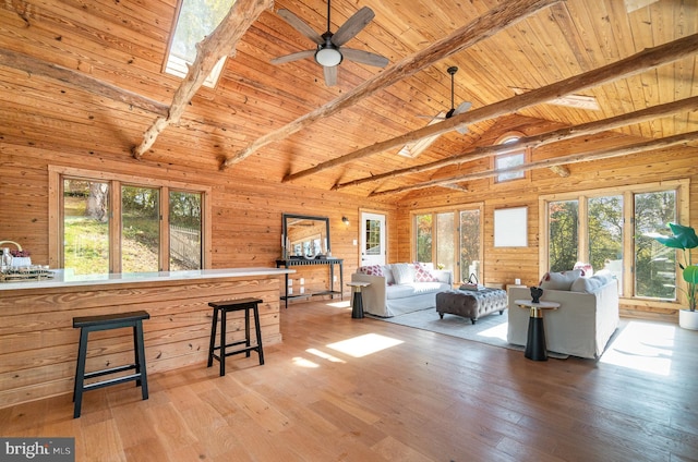 living room with wood walls, wood ceiling, ceiling fan, vaulted ceiling with skylight, and light hardwood / wood-style flooring