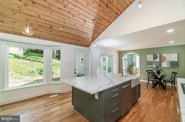 kitchen featuring sink, light wood-type flooring, an island with sink, decorative light fixtures, and light stone counters