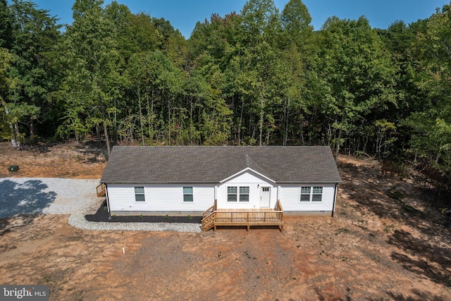 view of front of home featuring a forest view, driveway, a shingled roof, and a deck