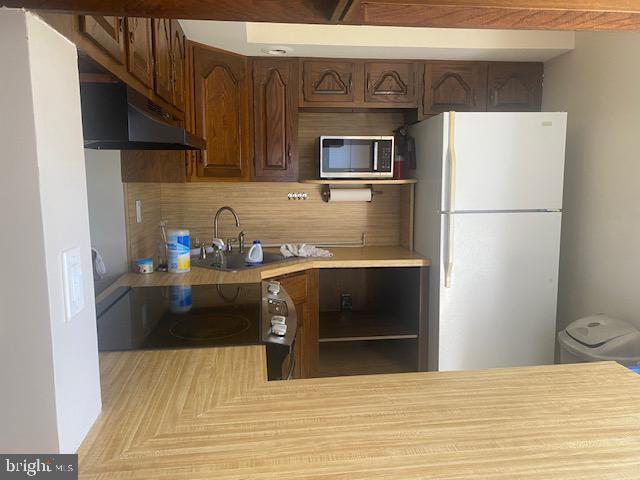 kitchen featuring dark brown cabinetry, sink, black range oven, white refrigerator, and decorative backsplash