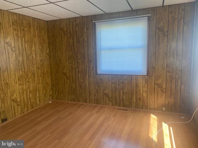 empty room featuring wooden walls, hardwood / wood-style floors, and a drop ceiling