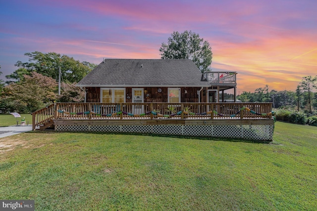 back of house at dusk featuring a yard, a deck, and a shingled roof