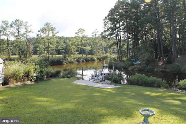 view of dock with a lawn, a forest view, and a water view