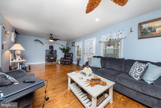 living area with a wood stove, wood finished floors, baseboards, and ceiling fan