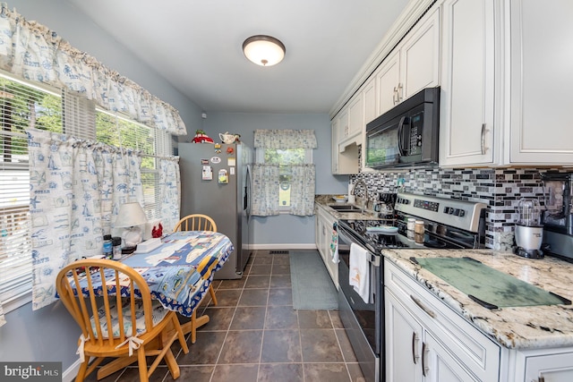 kitchen featuring baseboards, dark tile patterned flooring, a sink, appliances with stainless steel finishes, and tasteful backsplash