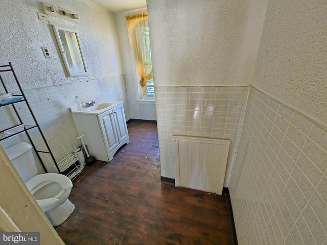 bathroom featuring toilet, hardwood / wood-style floors, vanity, radiator heating unit, and tile walls