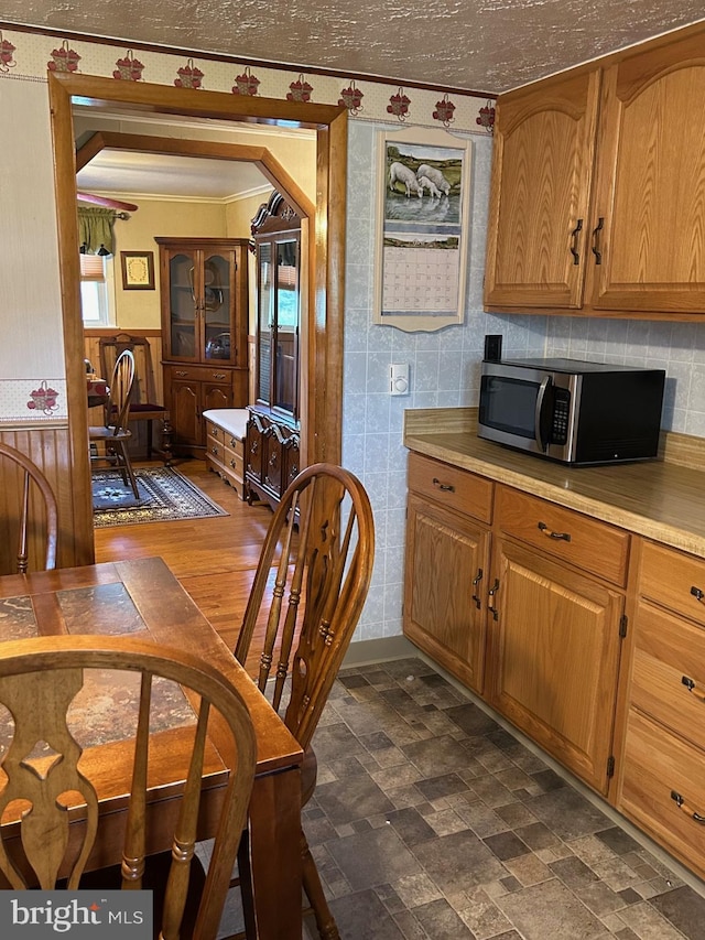 kitchen featuring stainless steel microwave, light countertops, brown cabinets, and ornamental molding