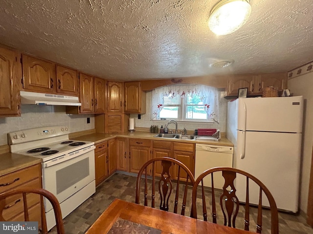 kitchen featuring a sink, under cabinet range hood, a textured ceiling, white appliances, and light countertops