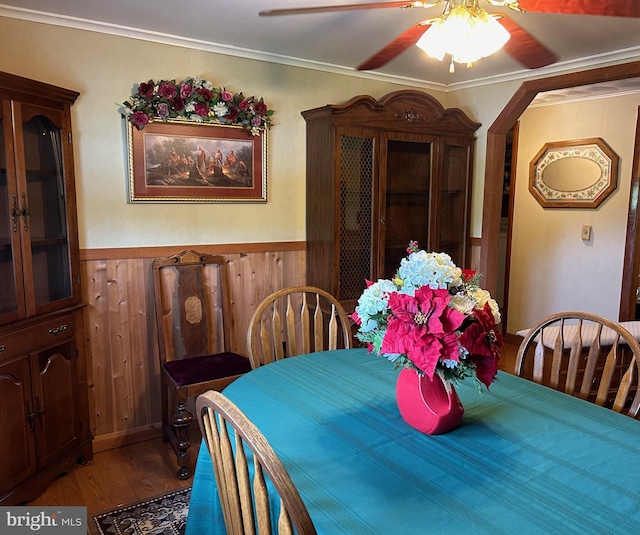 dining area with ornamental molding, wood finished floors, wood walls, wainscoting, and ceiling fan