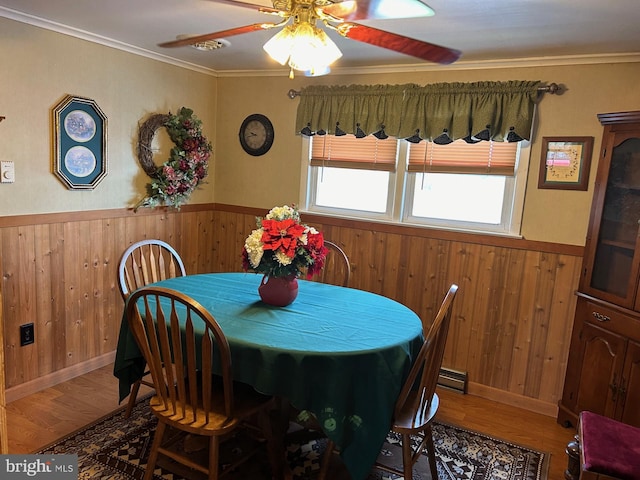 dining area featuring wooden walls, wainscoting, crown molding, and wood finished floors