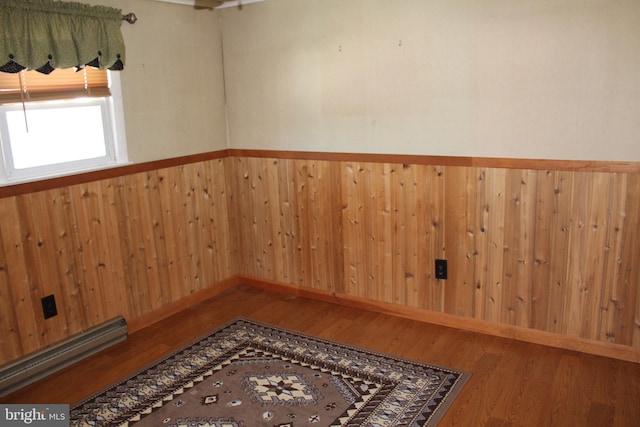 spare room with wood finished floors, a wainscoted wall, wood walls, and a baseboard radiator