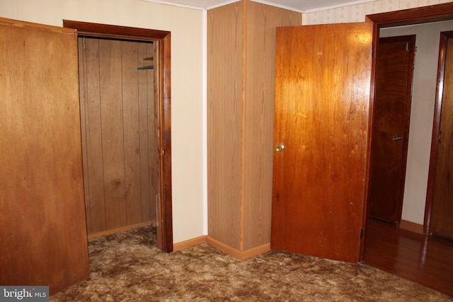 unfurnished bedroom featuring wood walls, dark carpet, and crown molding