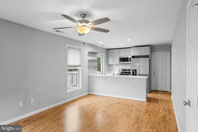 kitchen with gray cabinets, light hardwood / wood-style floors, kitchen peninsula, appliances with stainless steel finishes, and ceiling fan