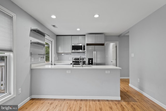 kitchen featuring appliances with stainless steel finishes, gray cabinetry, kitchen peninsula, light hardwood / wood-style flooring, and sink