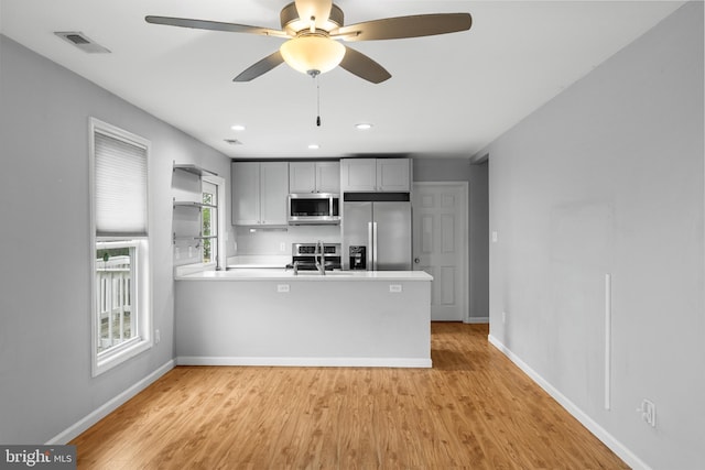 kitchen with gray cabinets, kitchen peninsula, light hardwood / wood-style flooring, appliances with stainless steel finishes, and ceiling fan