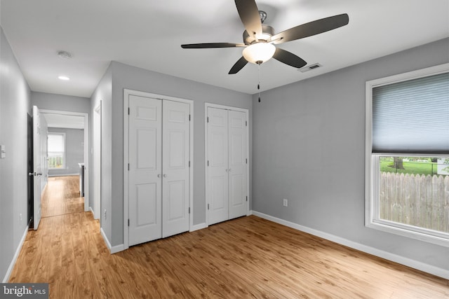 unfurnished bedroom featuring two closets, light hardwood / wood-style floors, and ceiling fan