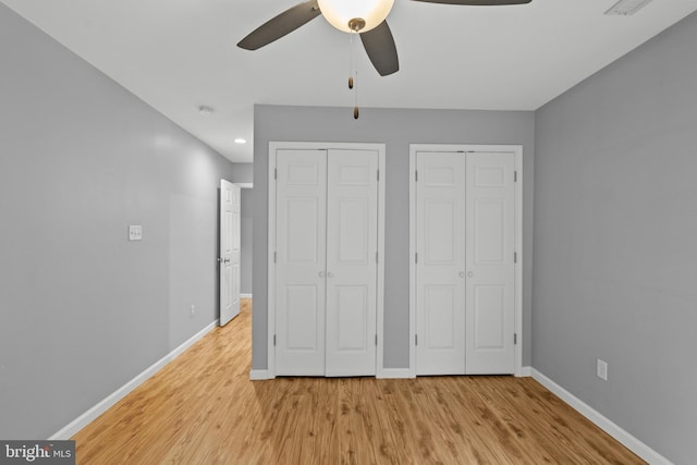 unfurnished bedroom featuring ceiling fan, multiple closets, and light hardwood / wood-style flooring