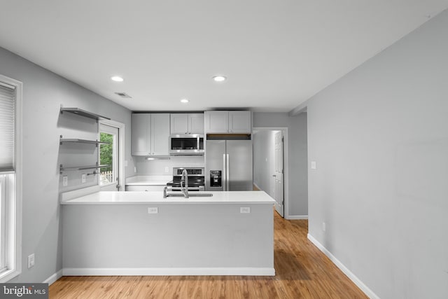 kitchen with sink, stainless steel appliances, kitchen peninsula, and light hardwood / wood-style flooring