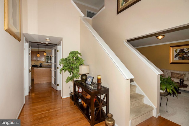 stairway with baseboards, wood finished floors, a towering ceiling, and ornamental molding