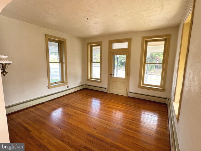 interior space with a textured ceiling, baseboard heating, and hardwood / wood-style flooring