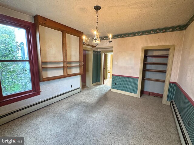 carpeted spare room featuring a textured ceiling, a baseboard heating unit, and a chandelier