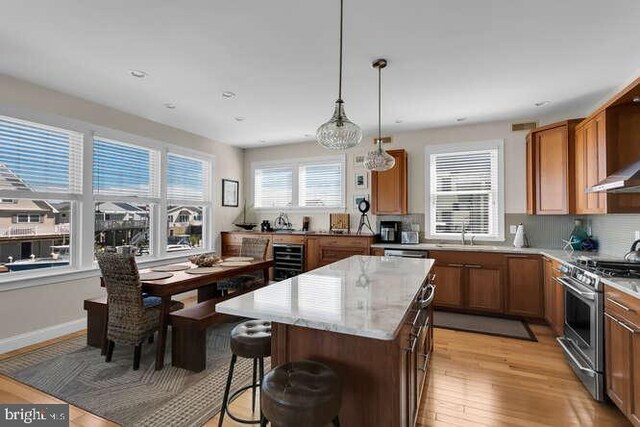 kitchen with wall chimney exhaust hood, stainless steel gas range, backsplash, and light stone counters