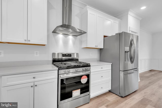 kitchen featuring wall chimney exhaust hood, stainless steel appliances, crown molding, light hardwood / wood-style flooring, and white cabinets