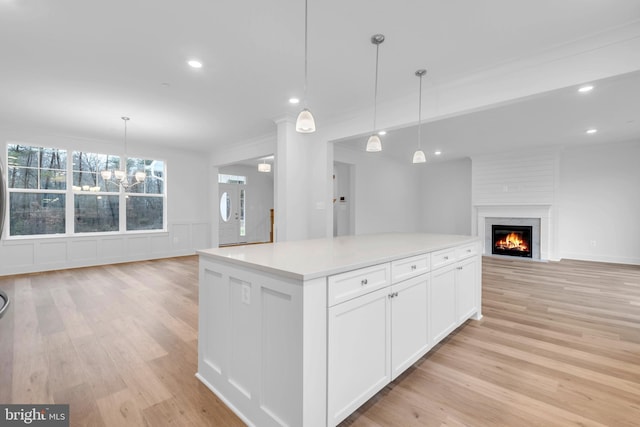 kitchen with hanging light fixtures, light hardwood / wood-style flooring, a fireplace, a kitchen island, and white cabinetry