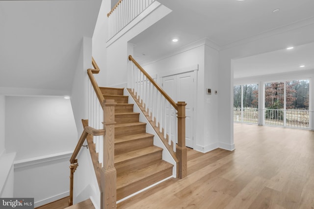 staircase with recessed lighting, wood finished floors, baseboards, and ornamental molding