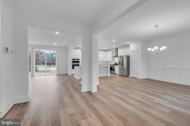 unfurnished living room featuring a chandelier, light wood-type flooring, ornamental molding, recessed lighting, and a decorative wall