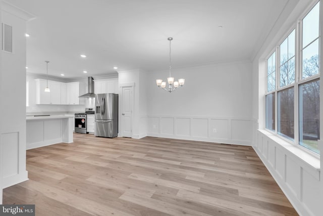 kitchen with wall chimney exhaust hood, stainless steel appliances, decorative light fixtures, white cabinets, and light wood-type flooring