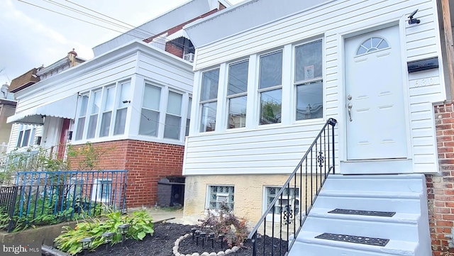 view of exterior entry featuring brick siding and fence