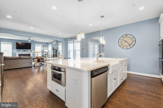 kitchen with dark wood-style floors, an island with sink, a fireplace, a sink, and dishwasher