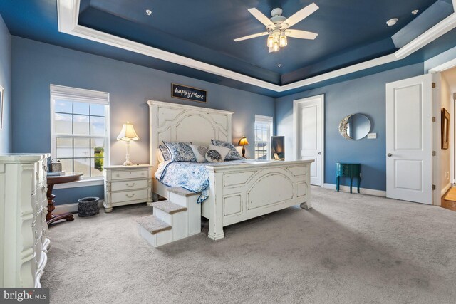 carpeted bedroom with multiple windows, a raised ceiling, baseboards, and a ceiling fan