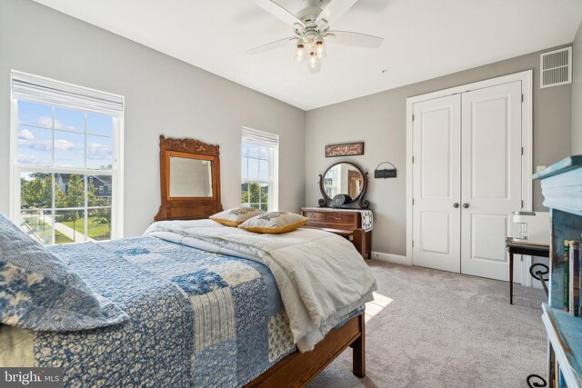 bedroom featuring a ceiling fan, visible vents, a closet, a glass covered fireplace, and light colored carpet