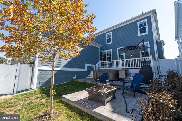 back of house featuring a fire pit, fence, a wooden deck, a lawn, and a gate