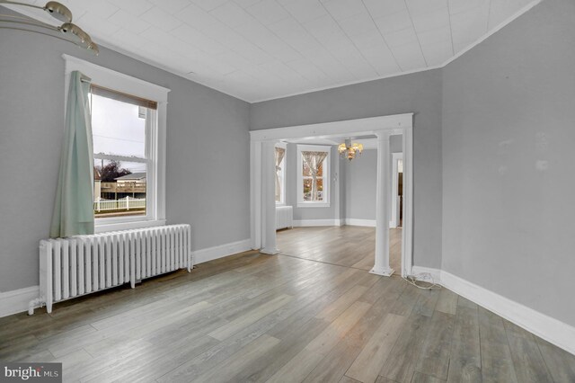 500 Dorsey Ave, Essex, MD 21221 - spare room featuring radiator heating unit, a chandelier, wood finished floors, ornate columns, and crown molding