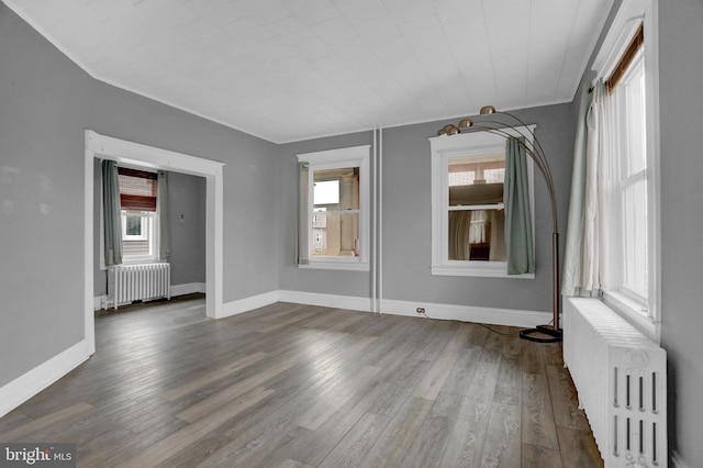 empty room with plenty of natural light, dark hardwood / wood-style flooring, and radiator heating unit