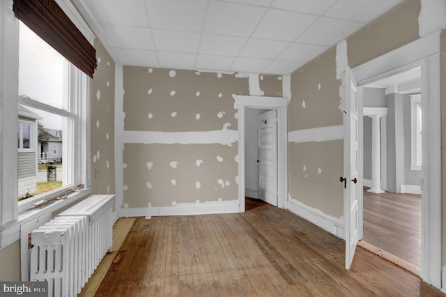 empty room with hardwood / wood-style floors, a paneled ceiling, and radiator